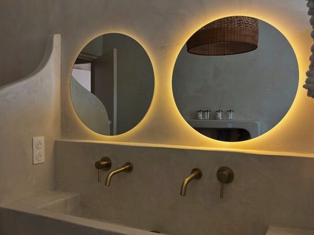 Salle de bain en béton ciré aux formes courbes, miroirs rétroéclairés et robinetterie laiton